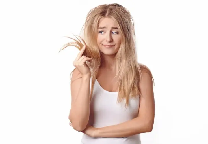 Mujer rubia con pelo poroso y enredado, tocándose un mechón con expresión de preocupación.