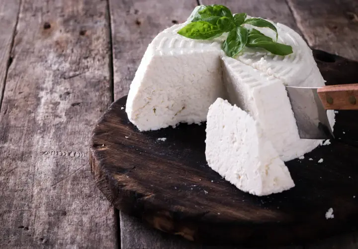 Ricotta fatta in casa, fresca e profumata, guarnita con basilico, pronta per essere gustata su un tagliere di legno rustico.