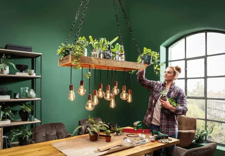 Frau dekoriert eine selbstgemachte Lampe mit Pflanzen. Ein DIY-Projekt für ein grünes Zuhause.