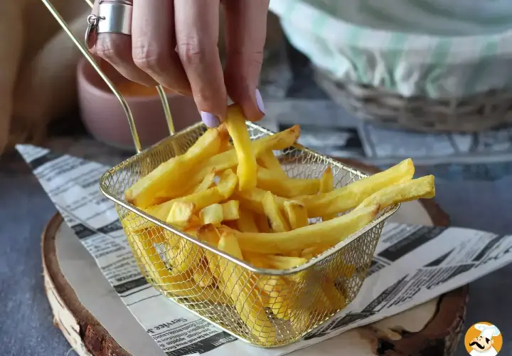 En hand plockar upp en gyllene pommes frites ur ett korgfat. Perfekt för en snabb aptitretare.