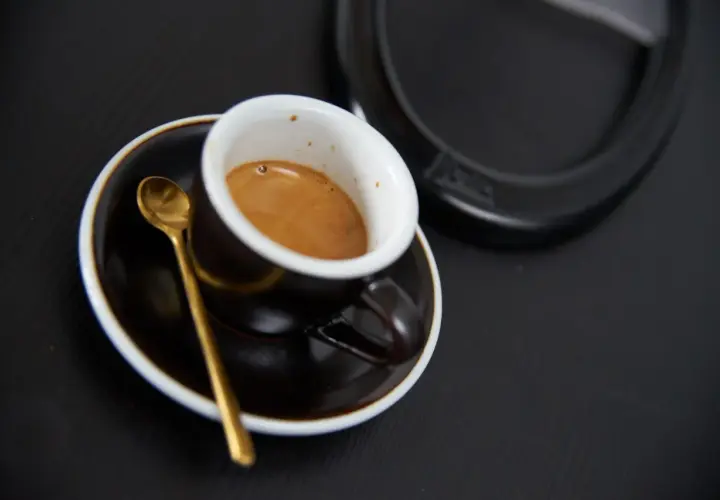 Aromatyczne włoskie espresso w filiżance z złotą łyżeczką na czarnym tle. Idealny początek dnia.