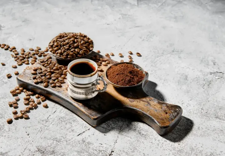 Chicco di caffè, macinato e bevanda scura su tagliere rustico. Chi dice che il caffè fa male, non ha visto questa meraviglia.