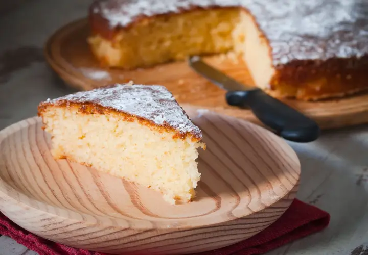 Una fetta di torta all'acqua soffice e spolverata di zucchero a velo su un piatto di legno.