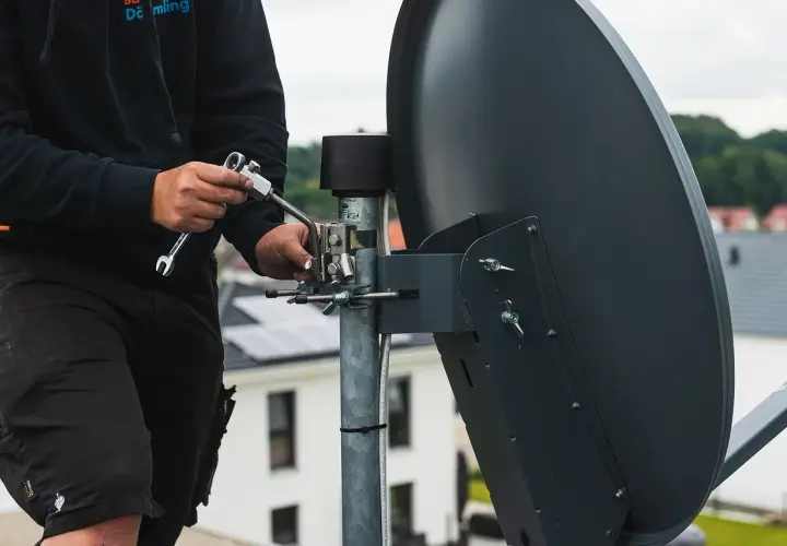 Instalator dokręca śruby przy antenie satelitarnej, pokazując jak ustawić antenę satelitarną cyfrowego polsatu.