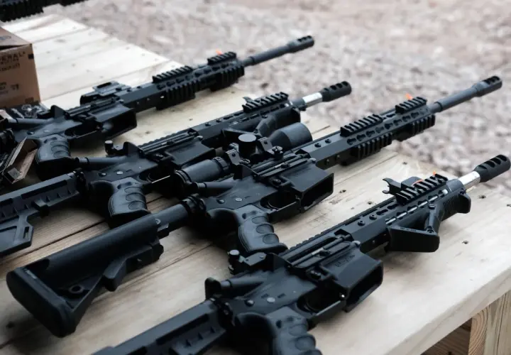 Kilka karabinów AR15 leży na drewnianym stole. W tle widać pudełko z amunicją.