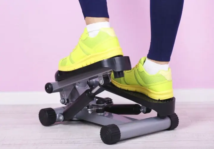 Osoba w neonowych butach ćwiczy na stepperze.