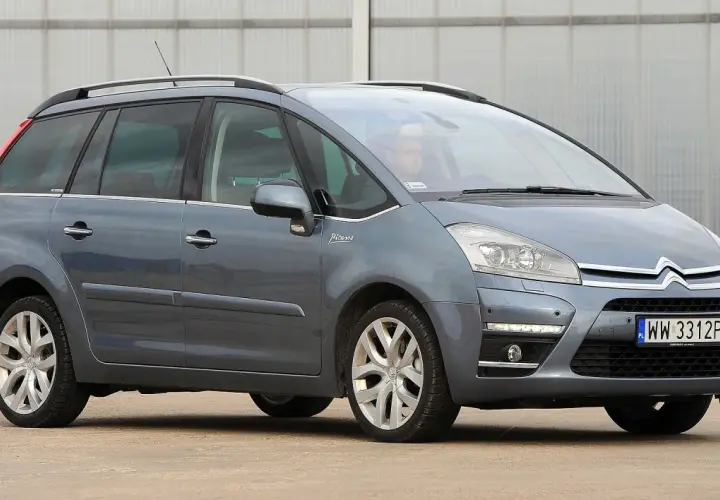 Szary Citroen C4 Grand Picasso 2.0 HDI z kierowcą za kierownicą, zaparkowany przed budynkiem.