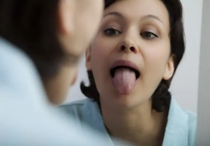 Donna si guarda allo specchio, mostrando la lingua. La saliva aiuta a digerire e a mantenere la bocca sana.