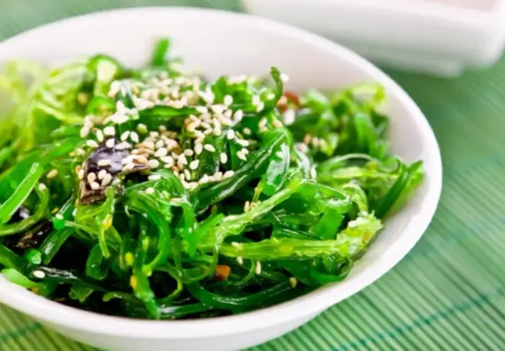A vibrant green seaweed salad, sprinkled with sesame seeds, perfect for healthy kelp recipes.