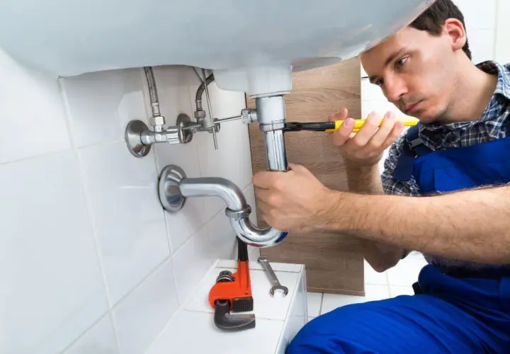 Monter instalacji sanitarnych dokręca kluczem syfon pod umywalką.