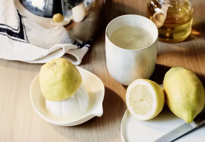 Zitronentee bei Halsschmerzen: frische Zitronen, ein Glas Tee und Honig auf einem Holztisch.