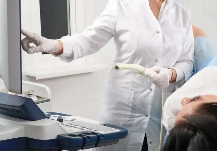Arzt führt eine Untersuchung mit einem Ultraschallgerät durch. Die Patientin liegt auf dem Tisch.