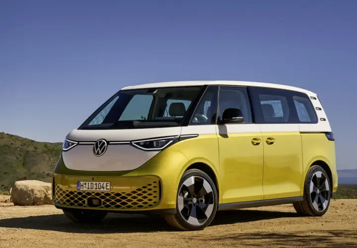 Minivan elettrico Volkswagen ID. Buzz bicolore giallo e bianco, parcheggiato su un terreno sterrato con sfondo di colline e cielo azzurro.