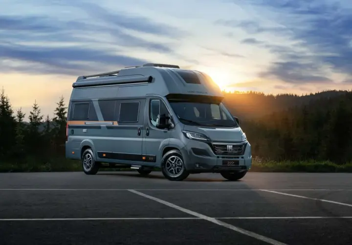 Nowe kampery Globe Traveller zapraszają na przygodę. Szary Fiat Ducato z nowoczesnym designem na tle zachodzącego słońca i lasu.