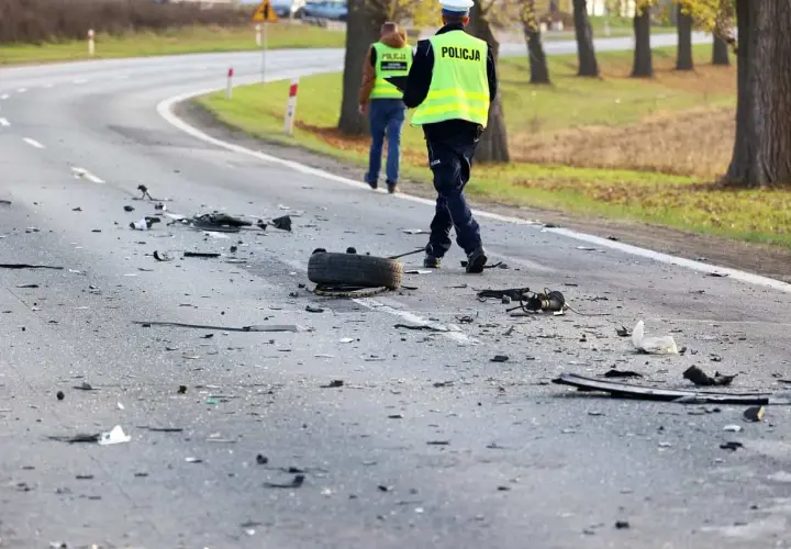 Na drodze po kolizji leżą szczątki, opona i elementy pojazdów. Policjanci w kamizelkach odblaskowych badają miejsce zdarzenia, być może szukając śladów ucieczki z miejsca kolizji.