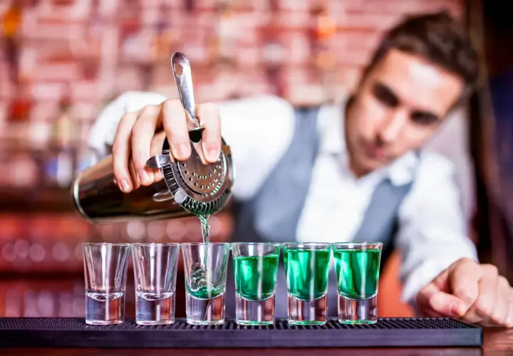 Barman nalewa zielony shot do kieliszków. Zastanawiasz się, ile zarabia barman na godzinę?