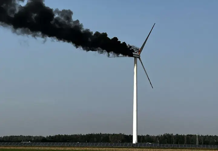 Płonąca turbina wiatrowa z gęstym, czarnym dymem unoszącym się na tle błękitnego nieba.