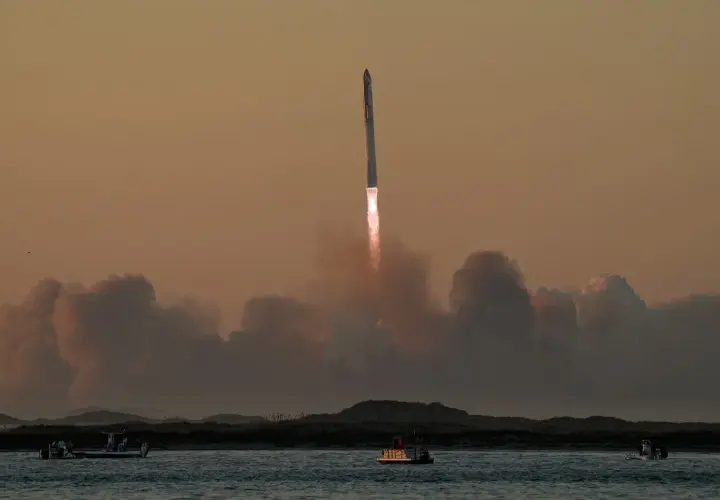 Starship start. Rakieta wznosi się w niebo, zostawiając za sobą kłęby dymu. Na wodzie widać łodzie obserwujące ten spektakularny widok.