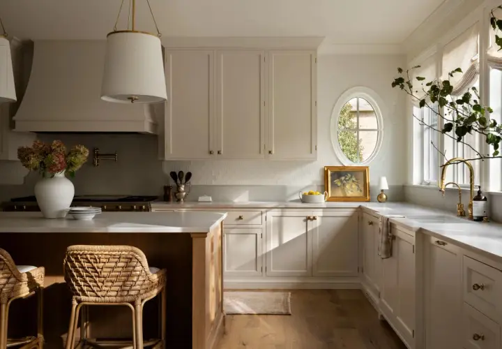 A bright, airy Studio McGee kitchen with cream cabinetry, a large island, woven stools, and a charming oval window.