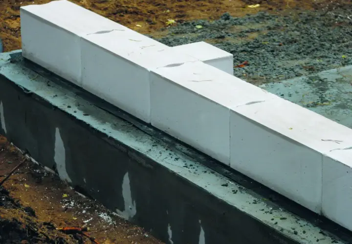 Białe bloczki z betonu komórkowego układane są na warstwie izolacji, tworząc fundament. Zaprawa zapewnia stabilność konstrukcji.