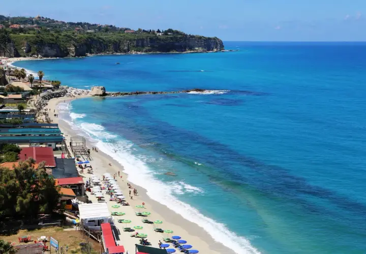 Plage animée à Tropea, Italie, avec des parasols colorés, des baigneurs et des falaises verdoyantes surplombant la mer d'un bleu éclatant.