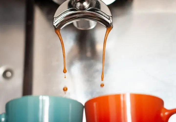 Gorące, aromatyczne espresso co to? Dwie strumienie kawy spływają do kolorowych filiżanek.