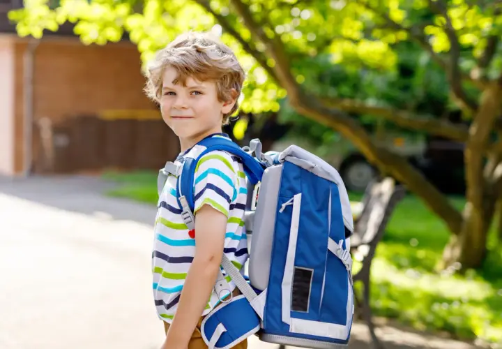 Niño sonriente con mochila azul, listo para ir al cole.