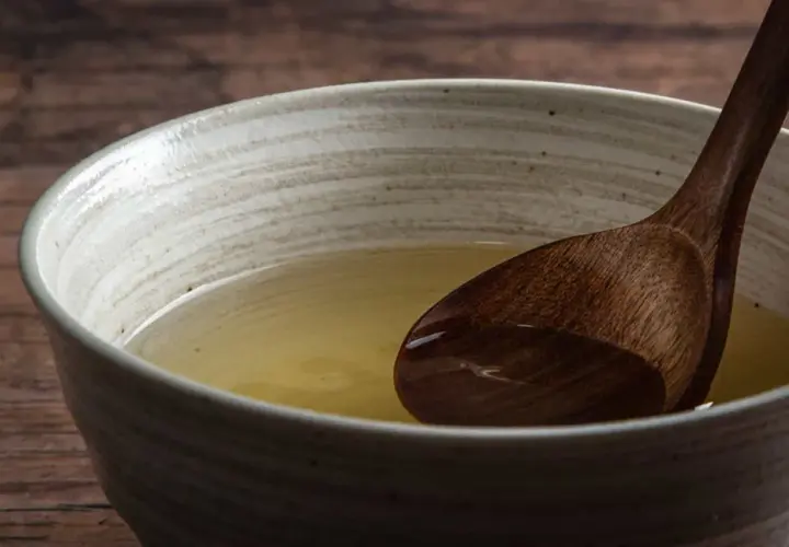 A wooden spoon rests in a bowl of clear, golden broth, hinting at the subtle flavors of various types of dashi.