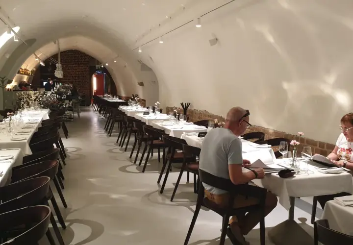 Elegancka sala restauracyjna z białymi obrusami i nakrytymi stołami. W tle bar. To może być najstarsza restauracja w Polsce.