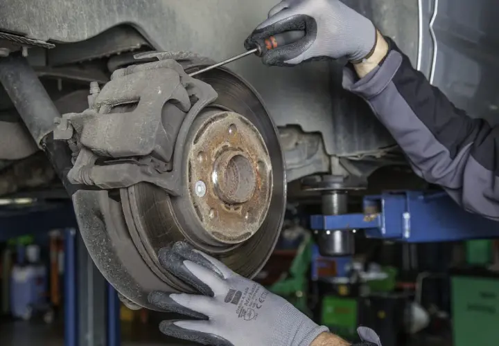 Mechanik w rękawiczkach sprawdza stan klocków hamulcowych przy tarczy hamulcowej samochodu.