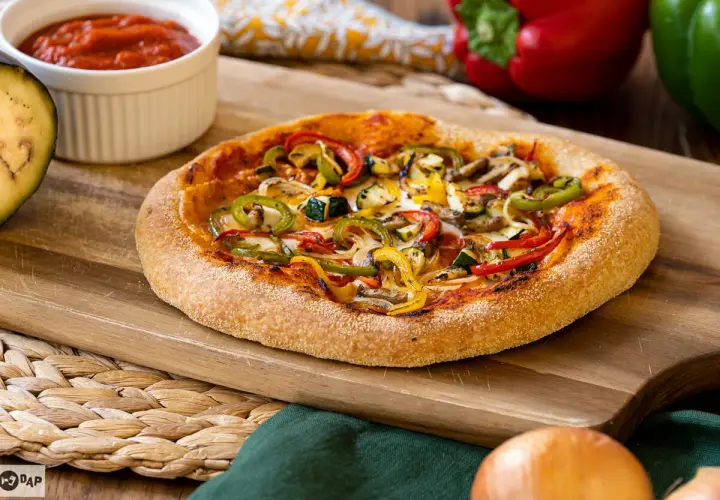 Pizza vegana con pimientos, calabacín y champiñones sobre tabla de madera. Salsa de tomate y berenjena al lado.