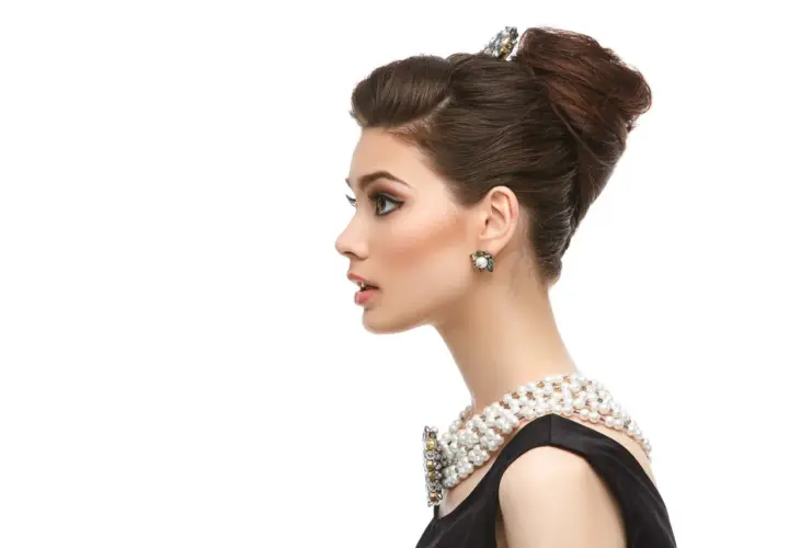 Elegante mujer con moño italiano, collar de perlas y pendientes llamativos.