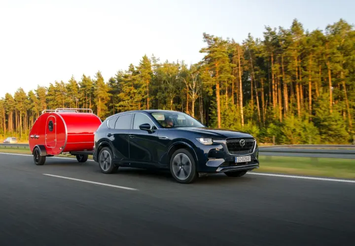 Ciemny SUV z czerwoną przyczepką typu teardrop jedzie po autostradzie. Zastanawiasz się, ile można jechać z przyczepką?