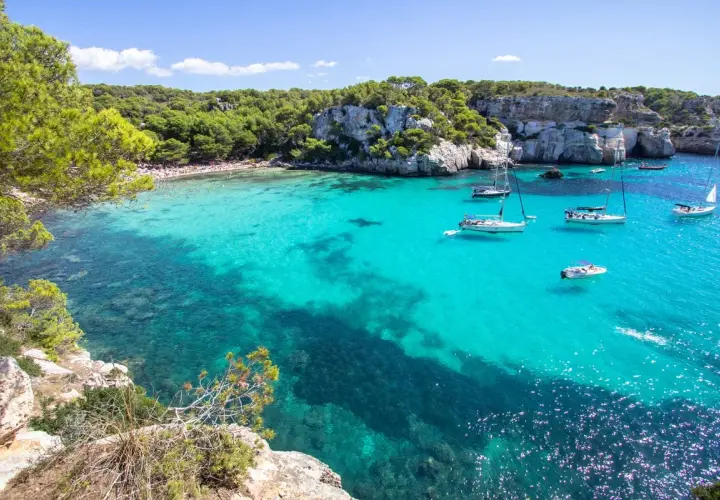 Calas turquesas y veleros, ideal para saber qué ver en Menorca en 3 días. Disfruta de playas paradisíacas y acantilados verdes.