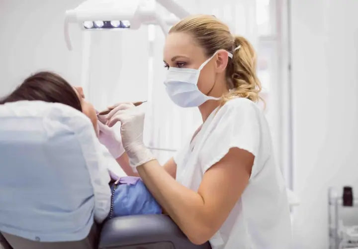 Dentista con mascherina esamina i denti di un paziente. La pulizia dei denti dura circa 30-60 minuti.