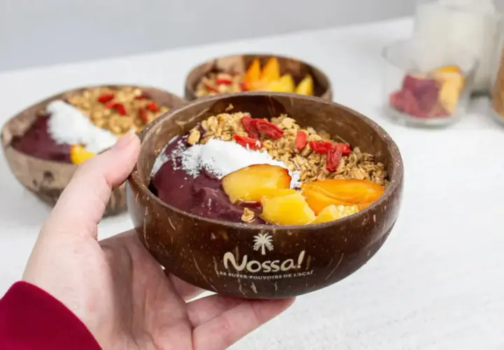Une main tient un bol en noix de coco rempli d'un délicieux acai bowl, garni de fruits frais, de granola et de baies de goji.