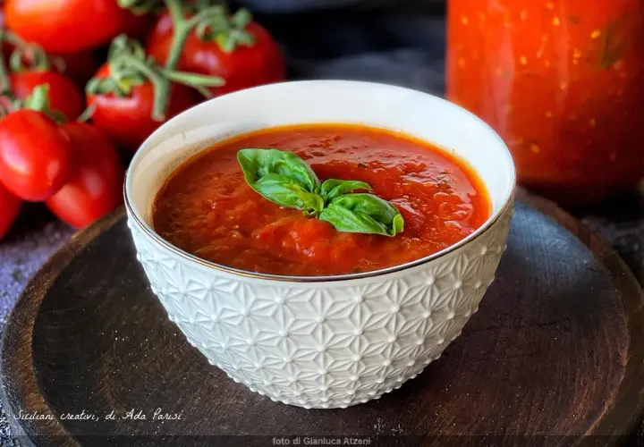 Una ciotola di salsa di pomodoro fatta in casa, guarnita con basilico fresco, con pomodori maturi sullo sfondo.