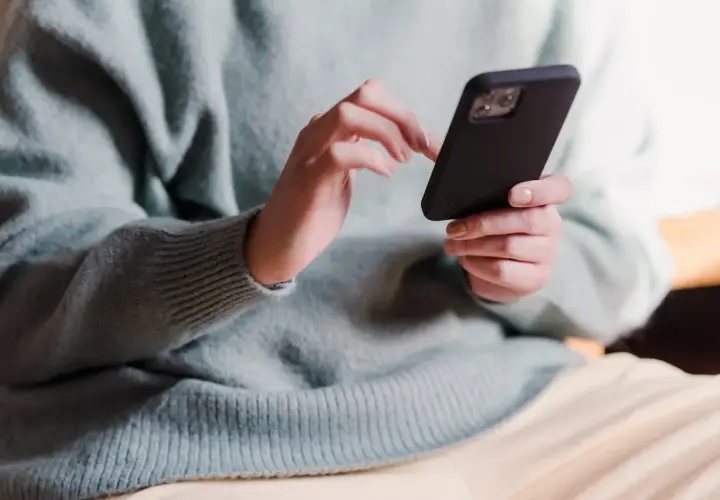 Dłonie w jasnym swetrze trzymają czarny telefon, wykonując skanowanie telefonu.