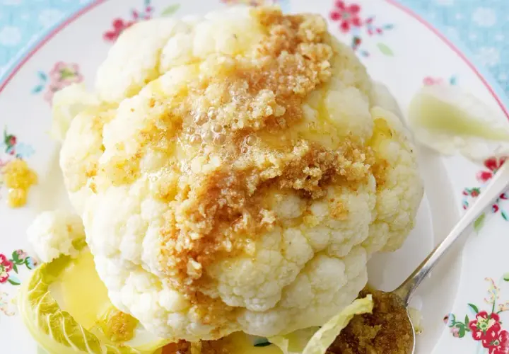 Ganzes Blumenkohlröschen mit Butter und Bröseln beträufelt, serviert auf einem Teller mit Blumenmuster. Tolle Idee für Blumenkohl Rezepte!