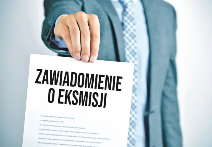 Mężczyzna w garniturze trzyma dokument z napisem "Zawiadomienie o eksmisji", sugerujący wstrzymanie eksmisji z mieszkania.