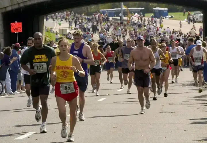 Uczestnicy biegną w maratonie, walcząc o jak najlepszy czas. Widać tłum biegaczy i kibiców.