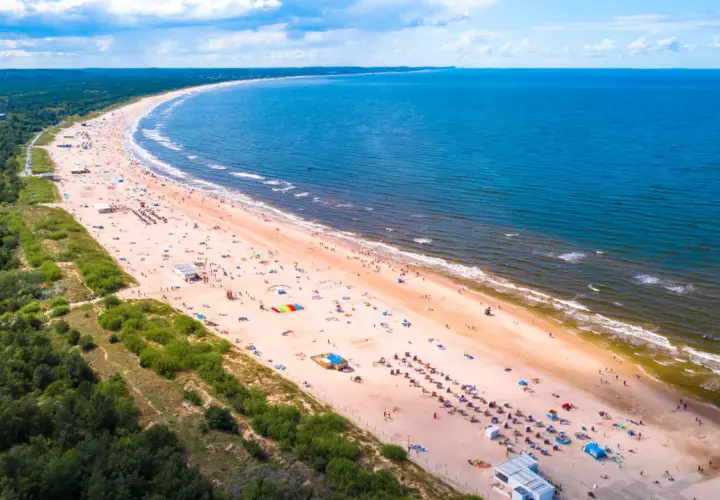 Słoneczne plaże nad morzem tętnią życiem. Tłumy plażowiczów odpoczywają na piasku, kąpią się w morzu i cieszą się wakacjami.