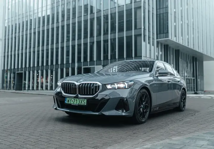 Eleganckie, szare BMW i5 z czarnymi felgami stoi przed nowoczesnym budynkiem biurowym.