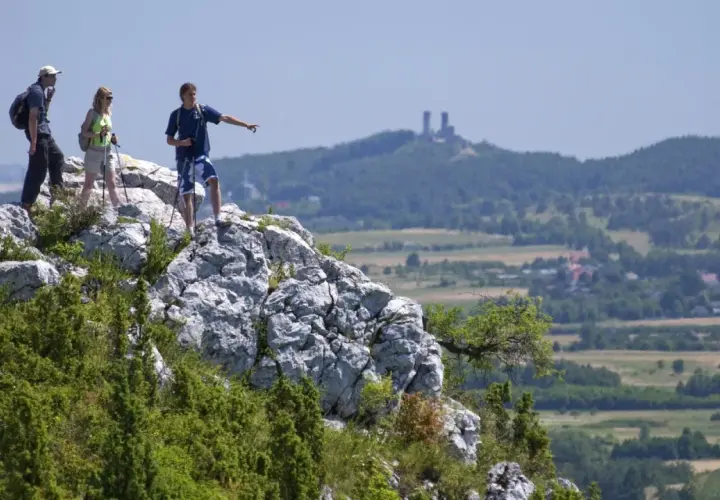Trzech turystów na skale w Górach Świętokrzyskich, jeden wskazuje kierunek. W oddali widać ruiny zamku.