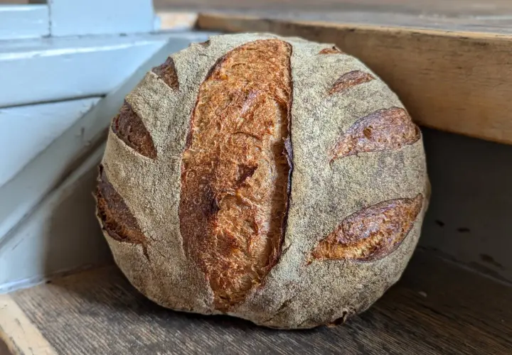 Ein goldbraunes Sauerteigbrot mit markanter Kruste und Einschnitten liegt auf einem Holzbrett. Die Frage "wie lange sauerteigbrot gehen lassen" beschäftigt Bäcker weltweit.