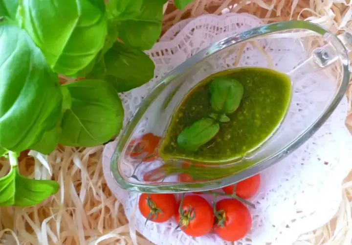 Aromatyczne pesto z bazylii w sosjerce, ozdobione listkami bazylii i pomidorkami koktajlowymi.