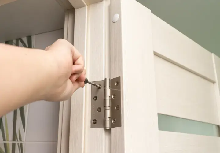 Dłoń dokręca śrubę zawiasu, regulując drzwi zewnętrzne. Trzy zawiasy zapewniają stabilność.