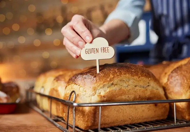 Dłoń wtyka tabliczkę "Gluten Free" w bochenek chleba. To przypomnienie, jak ważne jest, by wiedzieć, co robi gluten w organizmie, zwłaszcza przy wyborze pieczywa.