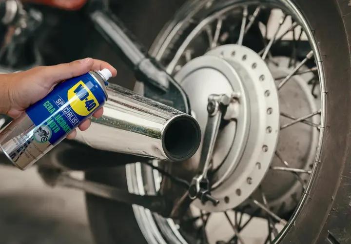 Mano che spruzza WD-40 su scarico cromato di moto. Un modo semplice per prendersi cura della cromatura e farla brillare.