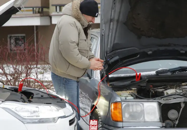 Mężczyzna podłącza kable rozruchowe do silnika samochodu.